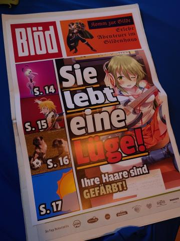 Eine Parodie-Zeitung der Bild, mit mehreren Elementen. Element 1: Ein Logo, das "Blöd"sagt. Element 2: "Komm zur Gilde, Erlebe Abenteurer im Gildenhaus". Element 3: 4 Bilder untereinander, die jeweils Angst aus Inside Out, Meliodas aus 7 Deadly Sins, Zwei Möpse (Hund) und eine bewölkte Wettervorhersage zeigen. Element 4: Ein Bild von Manami mit der übergroßen Beschriftung "Die lebt eine Lüge!" und der kleineren Beschriftung "Ihre Haare sind gefärbt." Manami hat auf dem Bild ihre üblichen grünen Haare.