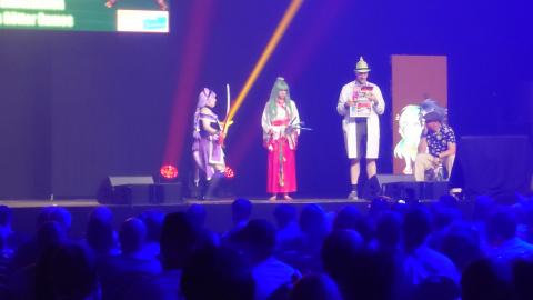 Hana-Chan, Manami und der Professor stehen auf der Bühne. Der Professer hat eine BLÖD in der Hand.
